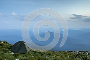 Summer camping in mountains at dawn. Tourist tent on round grass