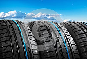 Summer car tires on over blue sky with clouds. Tire stack background. Car tyre protector close up. Black rubber tire. Brand new