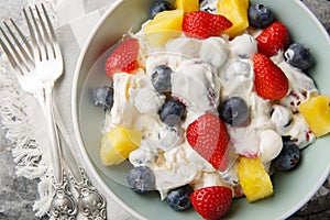 Summer cheesecake salad with strawberries, blueberries, pineapple, dressed with cream cheese and cream close-up in a bowl.