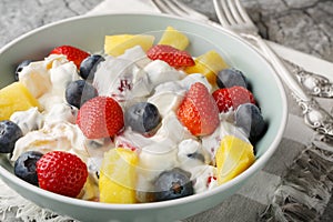 Summer cheesecake salad with strawberries, blueberries, pineapple, dressed with cream cheese and cream close-up in a bowl.