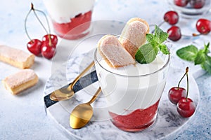 Summer cherry puff pastry with savoiardi cookies and cream cheese in glass on light grey background. Traditional tiramisu cake wit