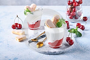 Summer cherry puff pastry with savoiardi cookies and cream cheese in glass on light grey background. Traditional tiramisu cake wit