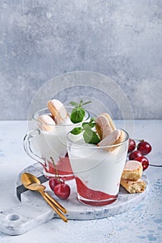 Summer cherry puff pastry with savoiardi cookies and cream cheese in glass on light grey background. Traditional tiramisu cake wit