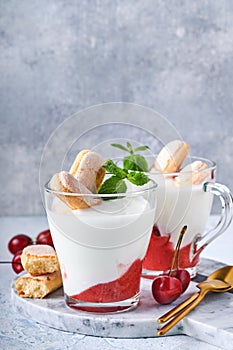 Summer cherry puff pastry with savoiardi cookies and cream cheese in glass on light grey background. Traditional tiramisu cake wit