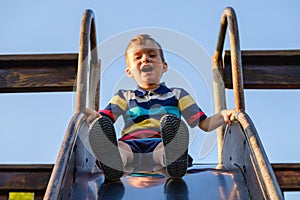 Summer, childhood, friendship and people concept - happy little boy on children playground slid from the hill
