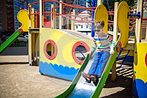 Summer, childhood, leisure, friendship and people concept - happy little boy on children playground slid from the hill