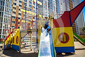 Summer, childhood, leisure, friendship and people concept - happy little boy on children playground slid from the hill