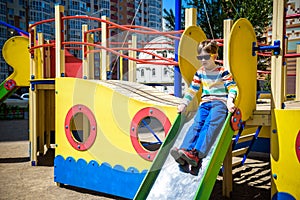 Summer, childhood, leisure, friendship and people concept - happy little boy on children playground slid from the hill