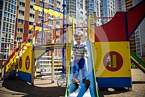 Summer, childhood, leisure, friendship and people concept - happy little boy on children playground slid from the hill