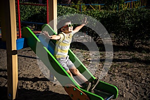 Summer, childhood, leisure, friendship and people concept - happy little boy on children playground slid from the hill