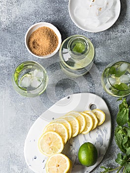 Summer citrus lemonade with ice in two bulging glasses, sugar in little white plate, slices of citrus on a ceramic white board and