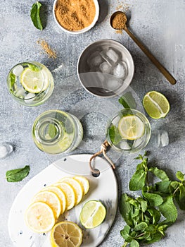 Summer citrus lemonade with ice in two bulging glasses, sugar in little white plate, slices of citrus on a ceramic white board and