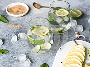 Summer citrus lemonade with ice in two bulging glasses, sugar in little white plate, slices of citrus on a ceramic white board on