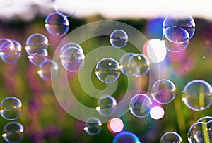 Summer clear green meadow with soap bubbles brightly shimmer and fly in the air at sunset