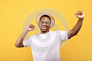 Summer clubbing. Young black guy dancing to favorite music with his hands up on yellow background