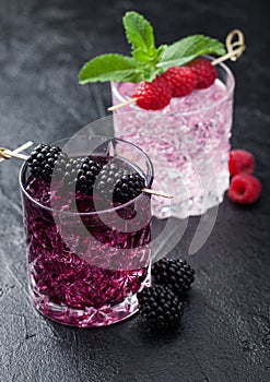 Summer cocktail with blackberry and pink lemonade in crystal glasses with ice cubes and mint on black background. Soda and alcohol