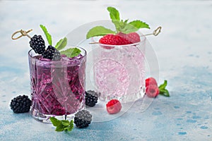 Summer cocktail with blackberry and pink lemonade in crystal glasses with ice cubes and mint on light blue background. Soda and