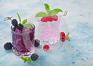 Summer cocktail with blackberry and pink lemonade in crystal glasses with ice cubes and mint on light blue background. Soda and