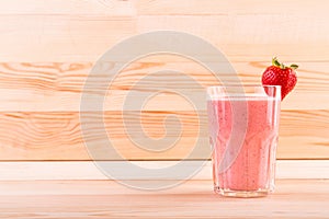 Summer cocktail from bright red strawberries and organic milk on a light brown wooden table. Strawberry smoothie in a glass.