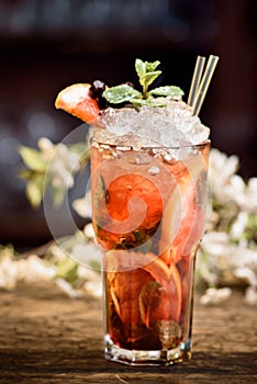 Summer cocktail with ice decorated with mint and berries on a wooden table on a floral background. berry mojito