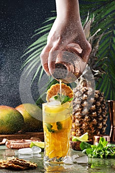 Summer cocktail with vodka, pineapple juice, mango, ice. Long drink or cold mocktail. Bartender pours drink from copper shaker,