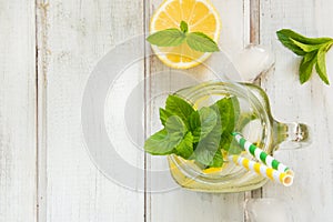 Summer cocktail, water detox with lemon, ice and mint in mason jar on a white wooden background. Top view.