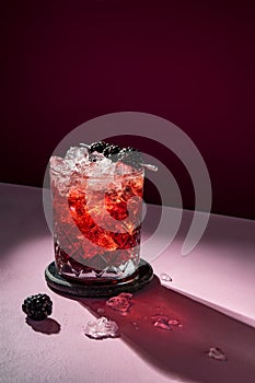 Summer cold cocktail drink with ice garnished with blackberry on dramatic violet