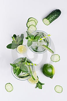 Summer cold drink with ice cubes, slices lime, cucumber, straw, twigs mint and ingredients on white wood board, top view.