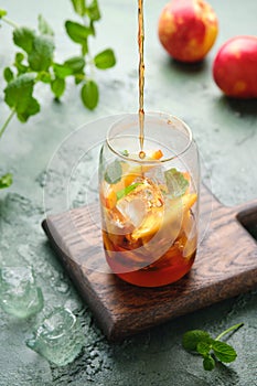 Summer cold drink, iced tea with nectarine or peach, ice and mint in a glass beaker on a green concrete background. Soft drinks,