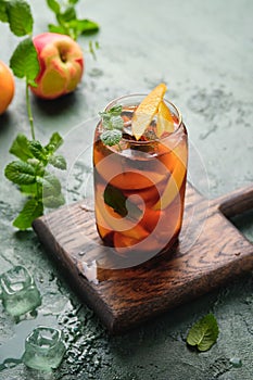 Summer cold drink, iced tea with nectarine or peach, ice and mint in a glass beaker on a green concrete background. Soft drinks,
