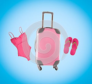 Summer collage with pink luggage, flip flops and swimsuit on blue background