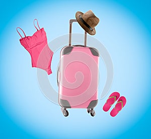 Summer collage with pink luggage , straw hat, flip flops and swimsuit on blue background