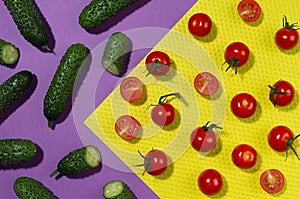 Summer color food background - red cherry tomatoes, green gherkin cucumber in sunlight with shadows on red and violet backdrop.