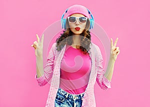 Summer colorful portrait stylish modern young woman listening to music in headphones posing on pink background