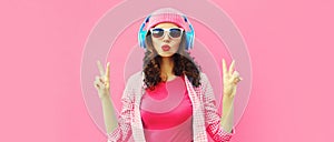 Summer colorful portrait of stylish modern young woman listening to music in headphones posing on pink background