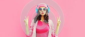 Summer colorful portrait of stylish modern young woman listening to music in headphones posing on pink background