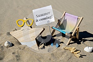 SUMMER IS COMING text on paper greeting card on background of beach chair lounge starfish summer vacation decor. Sandy