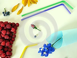 Summer composition installation - a glass of fresh raspberries, cocktail tubes, fresh flowers