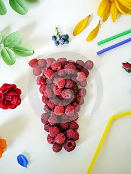 Summer composition installation - a glass of fresh raspberries, cocktail tubes, fresh flowers