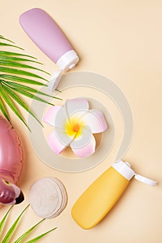 Summer composition with sunblock lotion bottles, palm leaf, sea shells and plumeria on pink background copy space Summer vacation