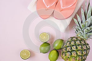 Summer composition. Tropical fruits and beach accessories - pineapple, coconut, lime, towel, flip-flops on pastel pink background