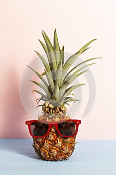 Summer concept about funny pineapple with sunglasses on blue wooden planks with pink background