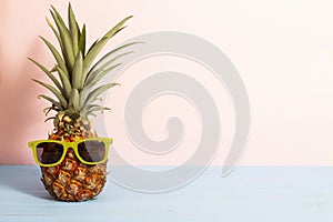 Summer concept about funny pineapple with sunglasses on blue wooden planks with pink background and copy space