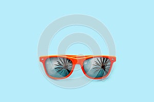 Summer concept image: orange sunglasses with palm tree reflections isolated in large pastel blue background.