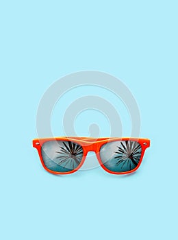 Summer concept image: orange sunglasses with palm tree reflections isolated in pastel blue background.