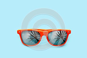 Summer concept image: orange sunglasses with palm tree reflections in pastel blue background.