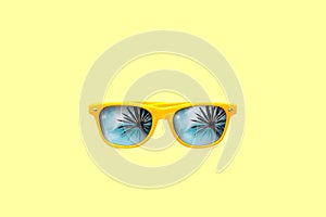 Summer concept image: yellow sunglasses with palm tree reflections isolated in large yellow background.