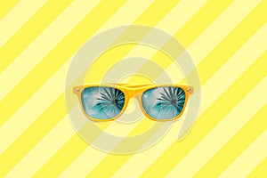 Summer concept image: yellow sunglasses with palm tree reflections isolated in large yellow striped background.