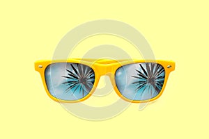 Summer concept image: yellow sunglasses with palm tree reflections isolated in pastel yellow background.