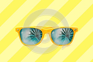 Summer concept image: yellow sunglasses with palm tree reflections isolated in pastel yellow striped background